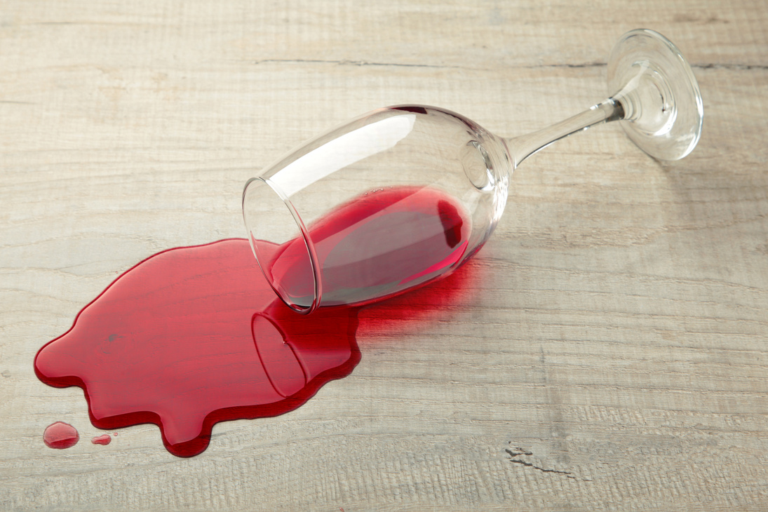 Glass of red wine fell on laminate, wine spilled on floor.